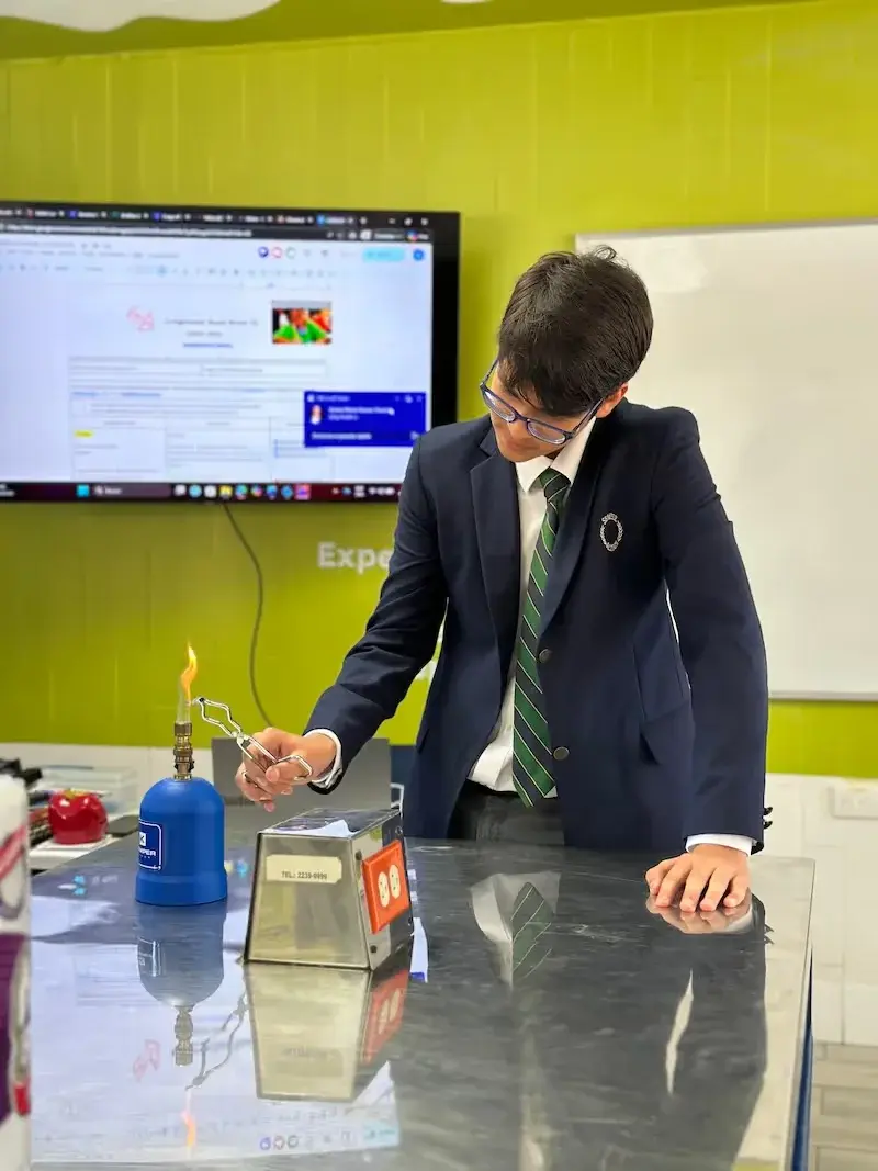 Estudiante realiza experimento científico con mechero de gas en laboratorio escolar frente a pantalla digital